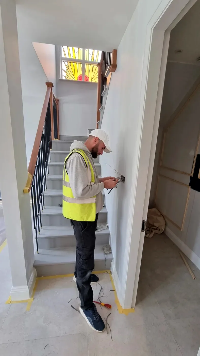 Electrician in a hi-vis vest fitting an accessory in a renovated stairwell