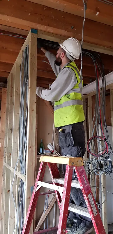 Electrician on a stepladder running new cables through a stud wall
