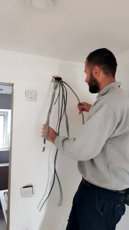 Electrician pulling new cables into a wall box during a rewire